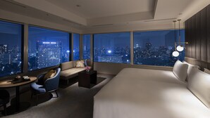 Habitación de hotel moderna con una cama grande, un sofá, un escritorio y vistas a un paisaje urbano por la noche.