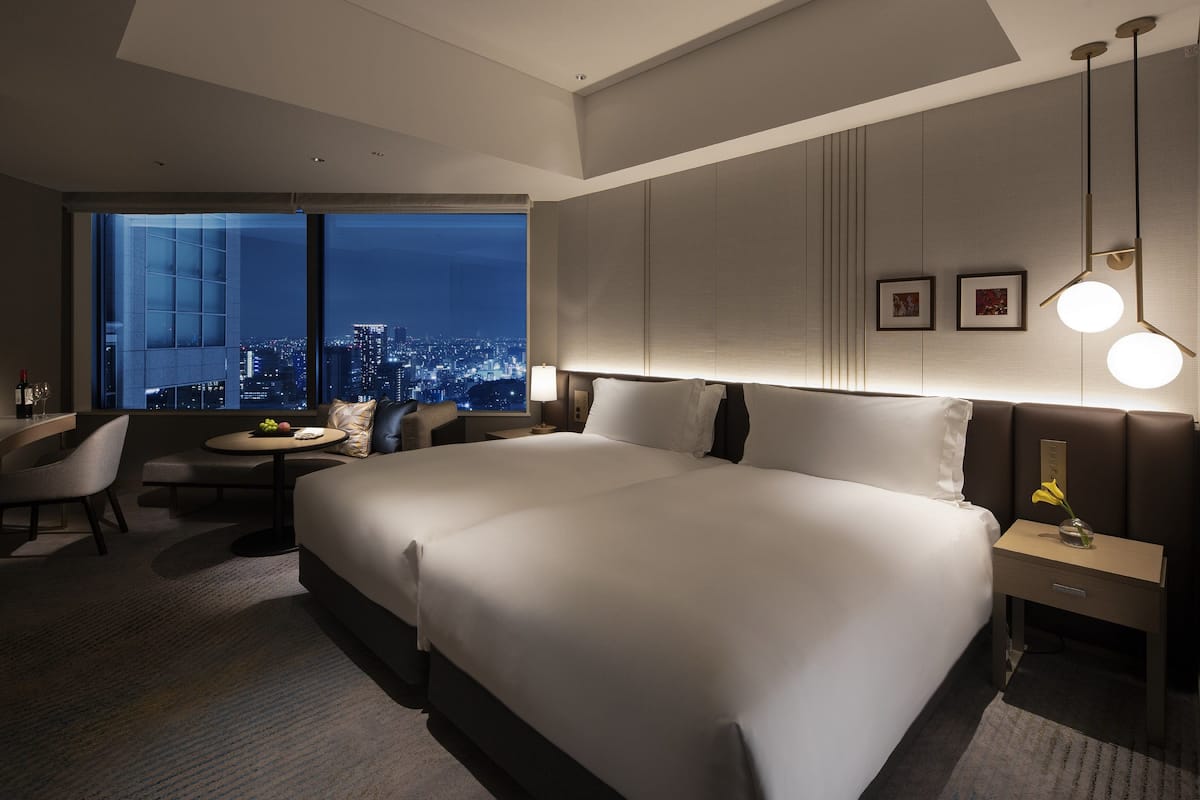 Une chambre d’hôtel moderne avec un grand lit, un bureau, une chaise et une vue sur la ville la nuit.