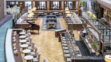 A spacious hotel lobby with a central seating area, a piano, and a bar.