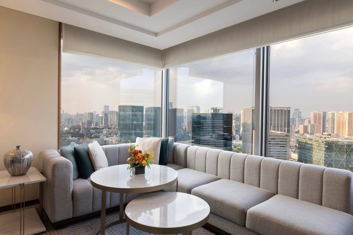 Un salon moderne doté d’un grand canapé d’angle, d’une table basse ronde et offrant une vue sur les gratte-ciel de la ville grâce à de grandes fenêtres.