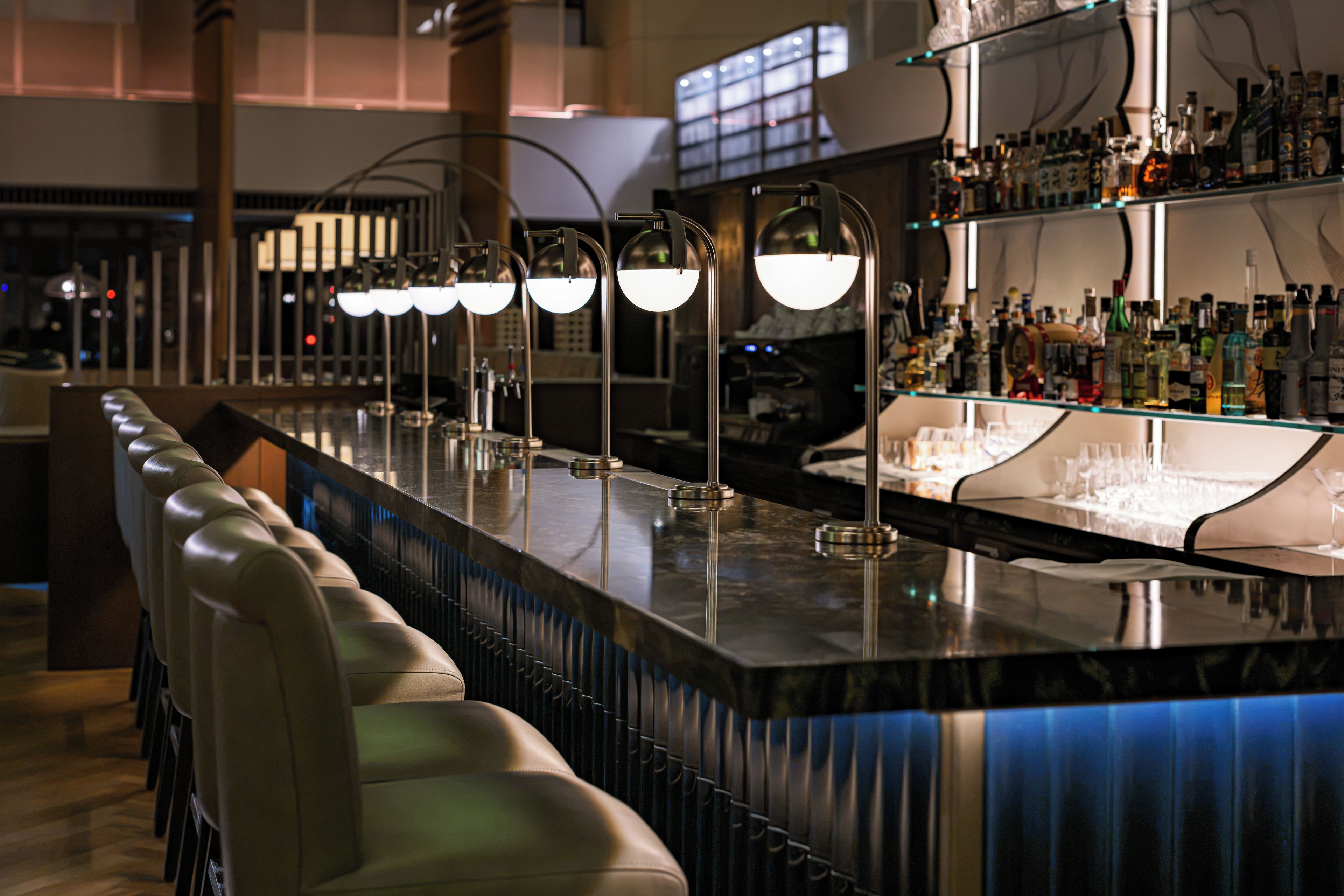 A bar area with a long counter, bar stools, and shelves stocked with bottles.