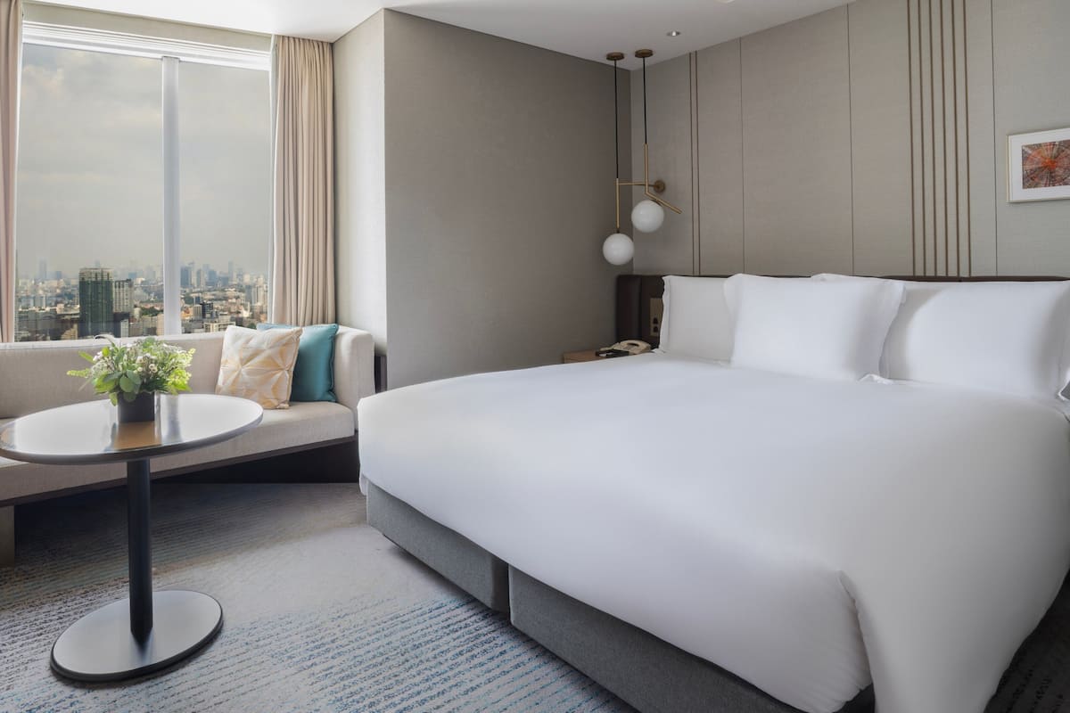 Une chambre d’hôtel avec un grand lit, un canapé, une petite table et une vue sur la ville.