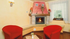 A cozy living room with a fireplace, two red armchairs, and a window with curtains. - Hotel Conca Verde (Zone)