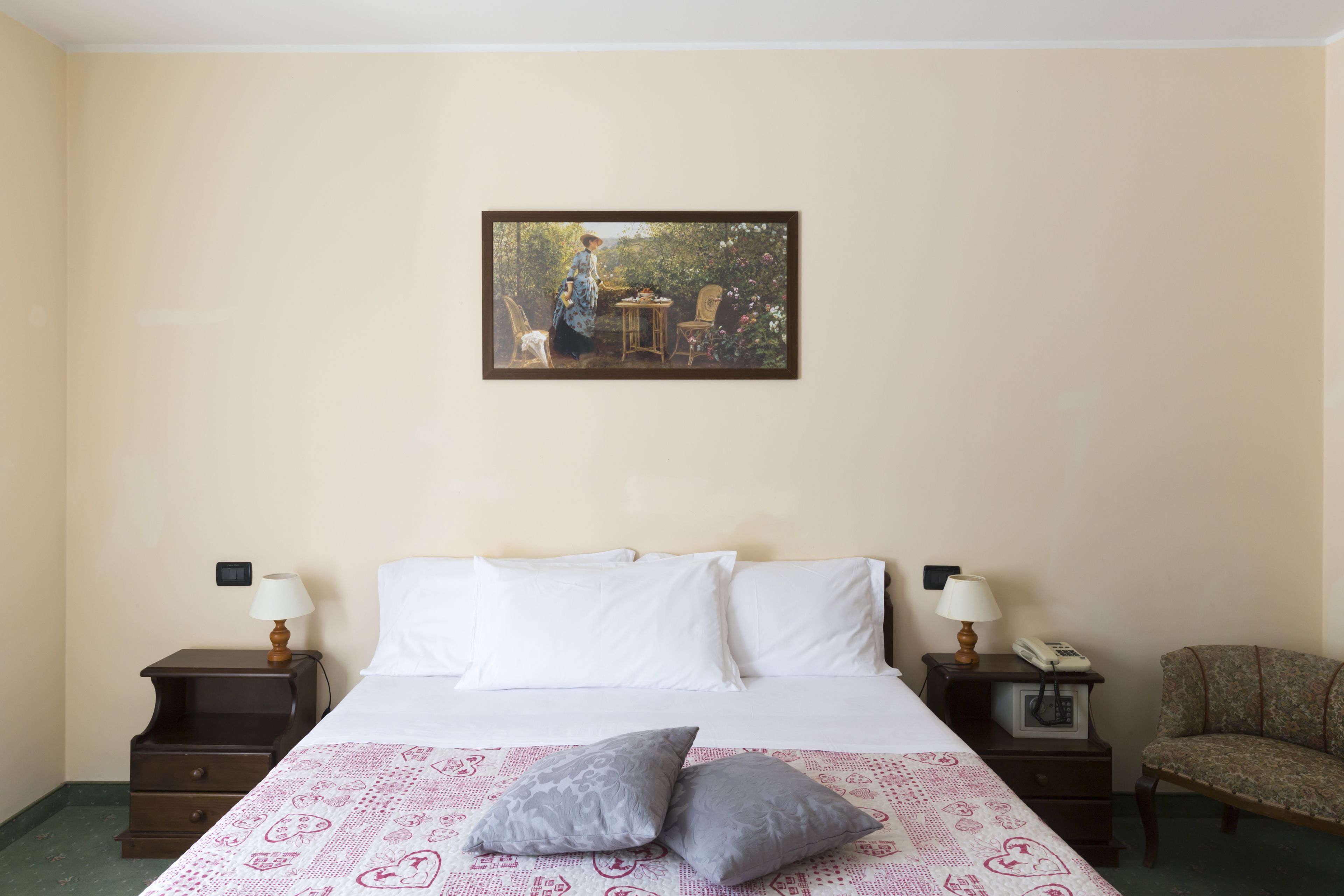 Een hotelkamer met een bed, twee nachtkastjes, een stoel, een schilderij en een telefoon.