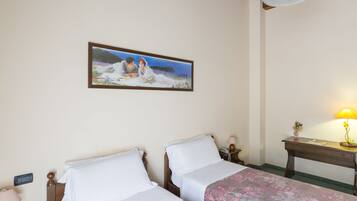 A hotel room with two beds, a painting on the wall, a bedside table with a lamp, and a wooden headboard.