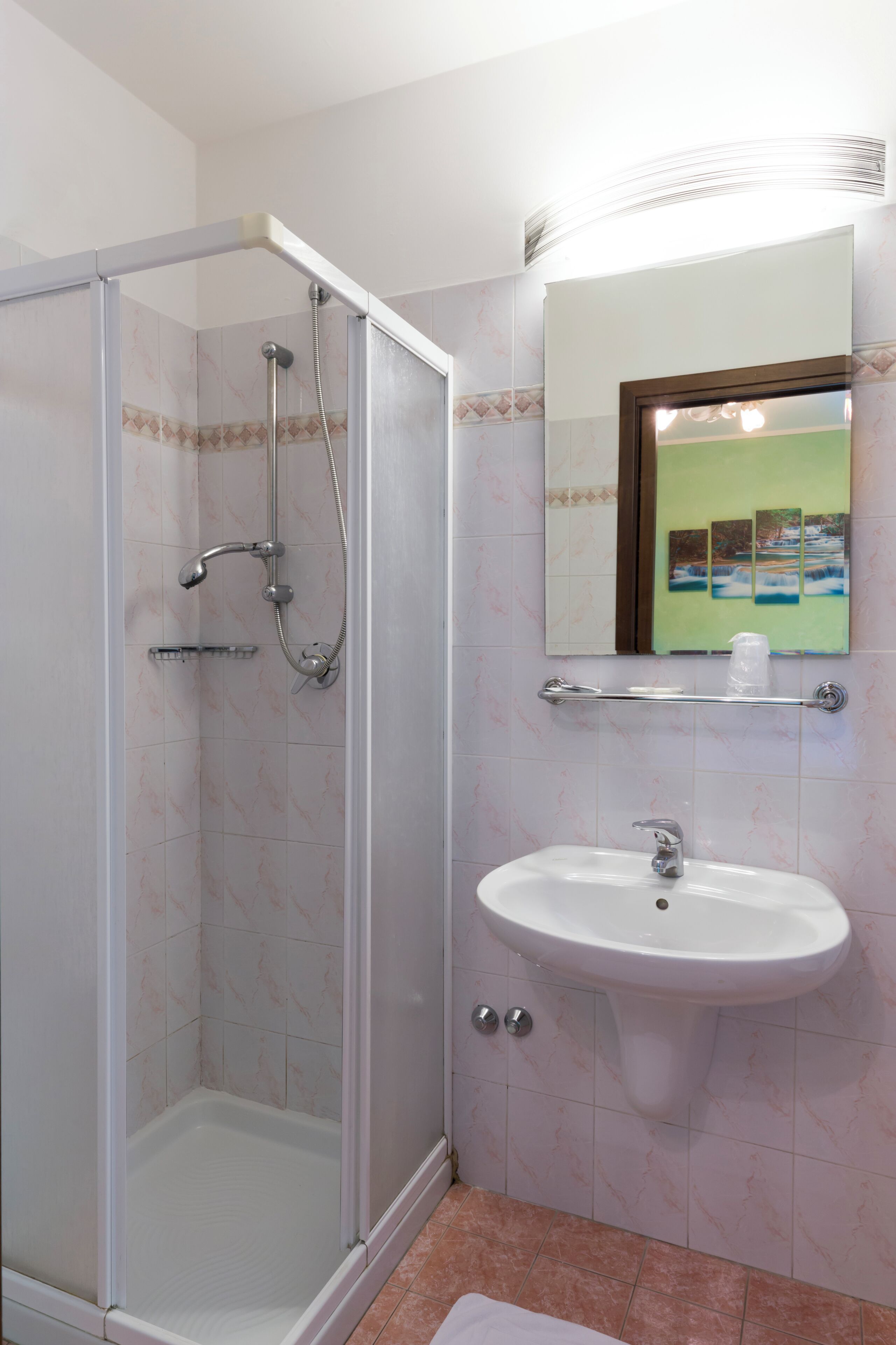Baño con ducha de vidrio, lavabo blanco y espejo sobre él.