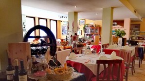 A restaurant with multiple tables set for dining, a wine rack, and various kitchen appliances in the background. - Hotel Conca Verde (Zone)