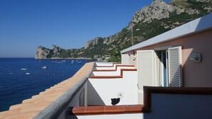 Un bâtiment situé sur la côte, doté d’un balcon donnant sur la mer et ayant une chaîne de montagnes en arrière-plan.