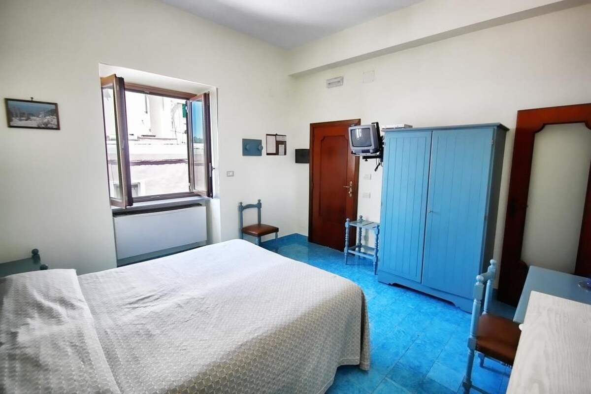 A room with a bed, a desk, a chair, a wardrobe, a television, and a window.