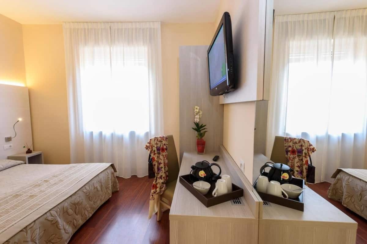 Una habitación de hotel con dos camas, un escritorio con espejo, televisión y ventana con cortinas.