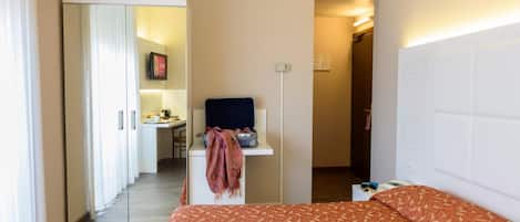 Une chambre d’hôtel avec un lit, un bureau et une chaise. On y trouve une porte donnant accès à une salle de bain et à un couloir.