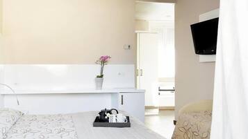 Hotelkamer met een bed, nachtkastje met bloevas, dienblad met spullen, televisie aan de muur en een deur naar een andere kamer.