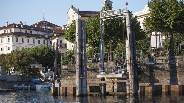A waterfront area with a sign reading "ISOLA BELLA" and a building labeled "RESTAURANTE DELFI" in the background. - Hotel Primavera (Stresa)