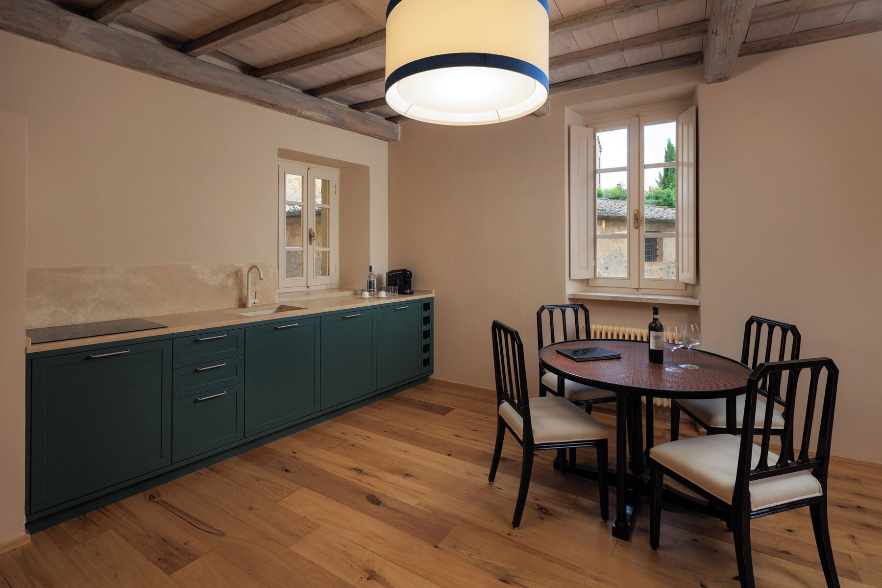 A kitchen with a wooden floor, a dining table with chairs, a window, and a pendant light.