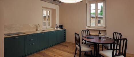 A kitchen with a wooden floor, a dining table with chairs, a window, and a pendant light.