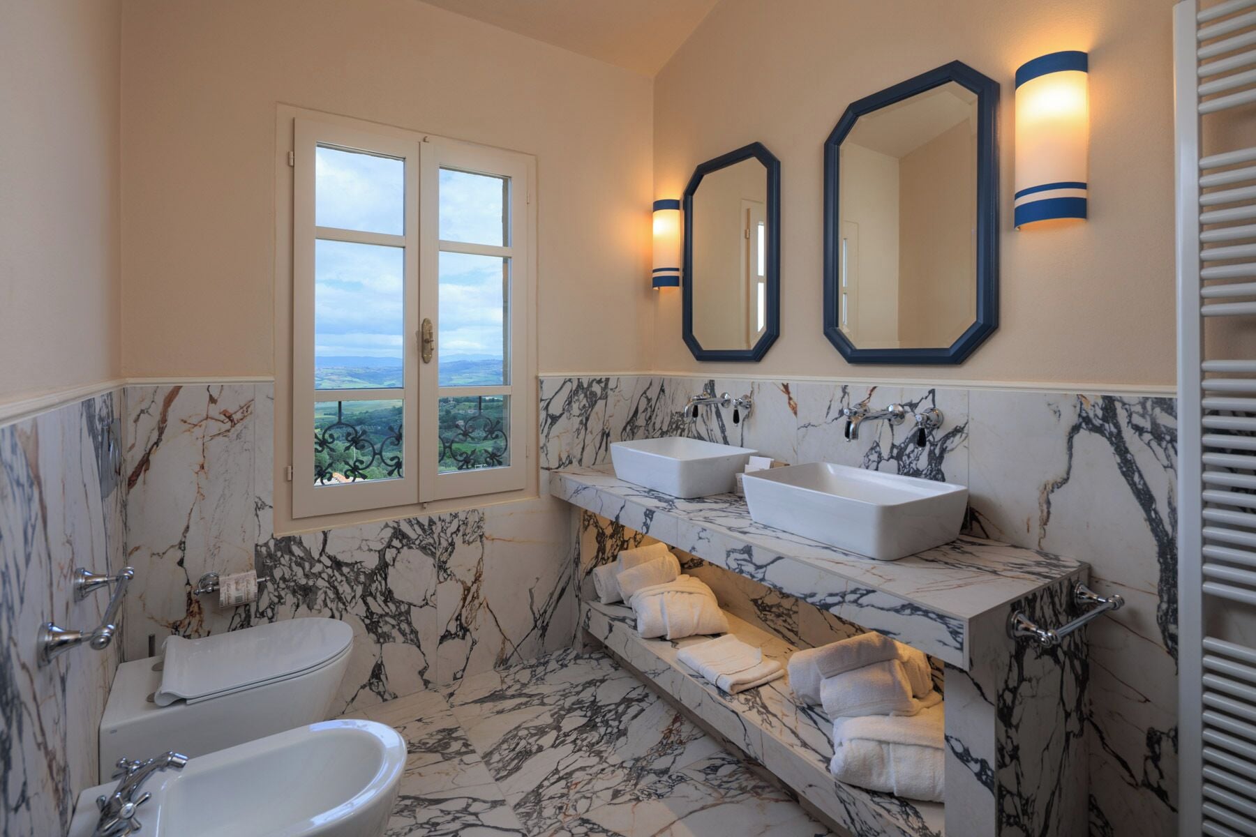 A bathroom with a bathtub, a toilet, a sink, two mirrors, and a window with a view.