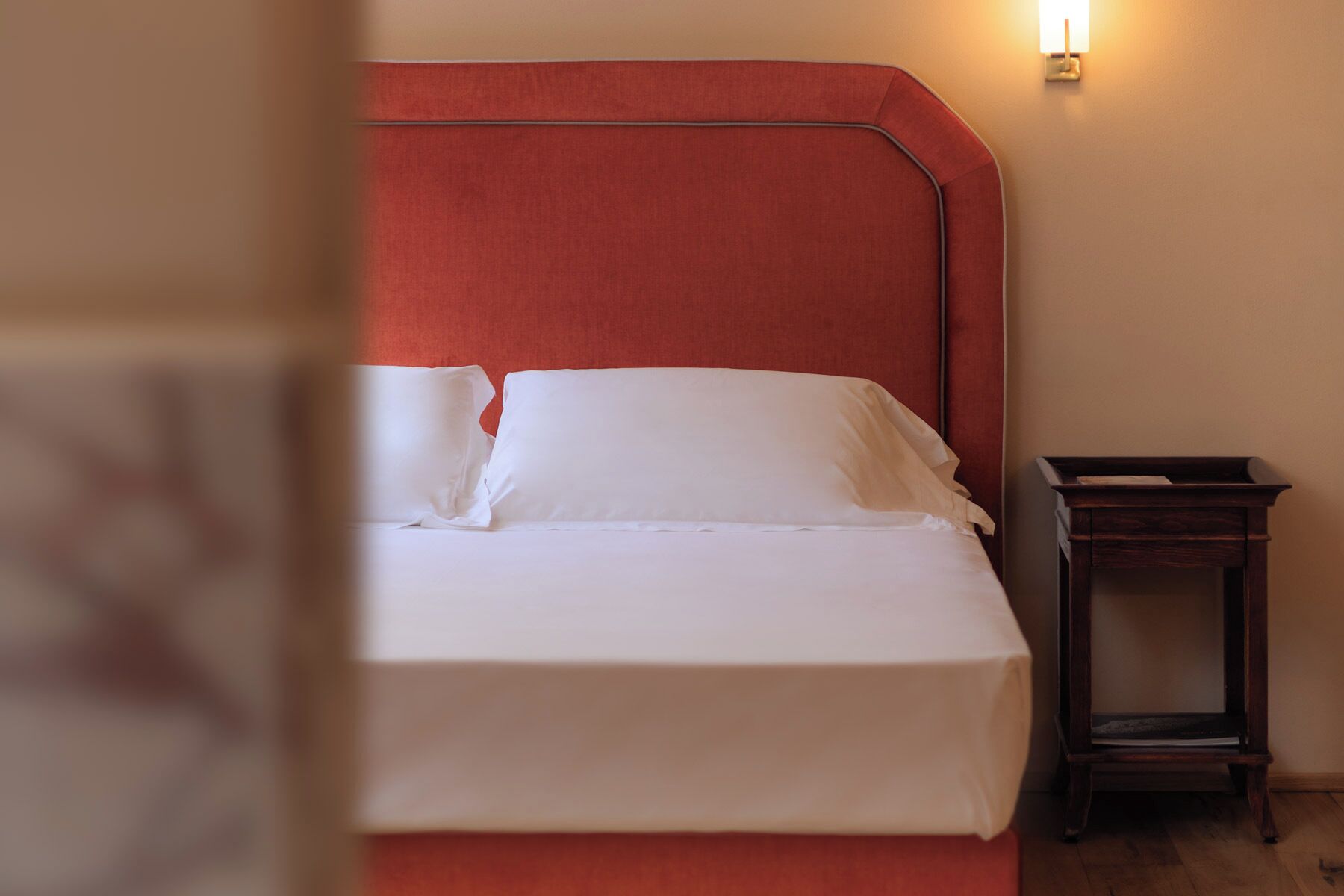 A neatly made bed with white linens, a wooden nightstand beside it, and a wall-mounted light fixture.