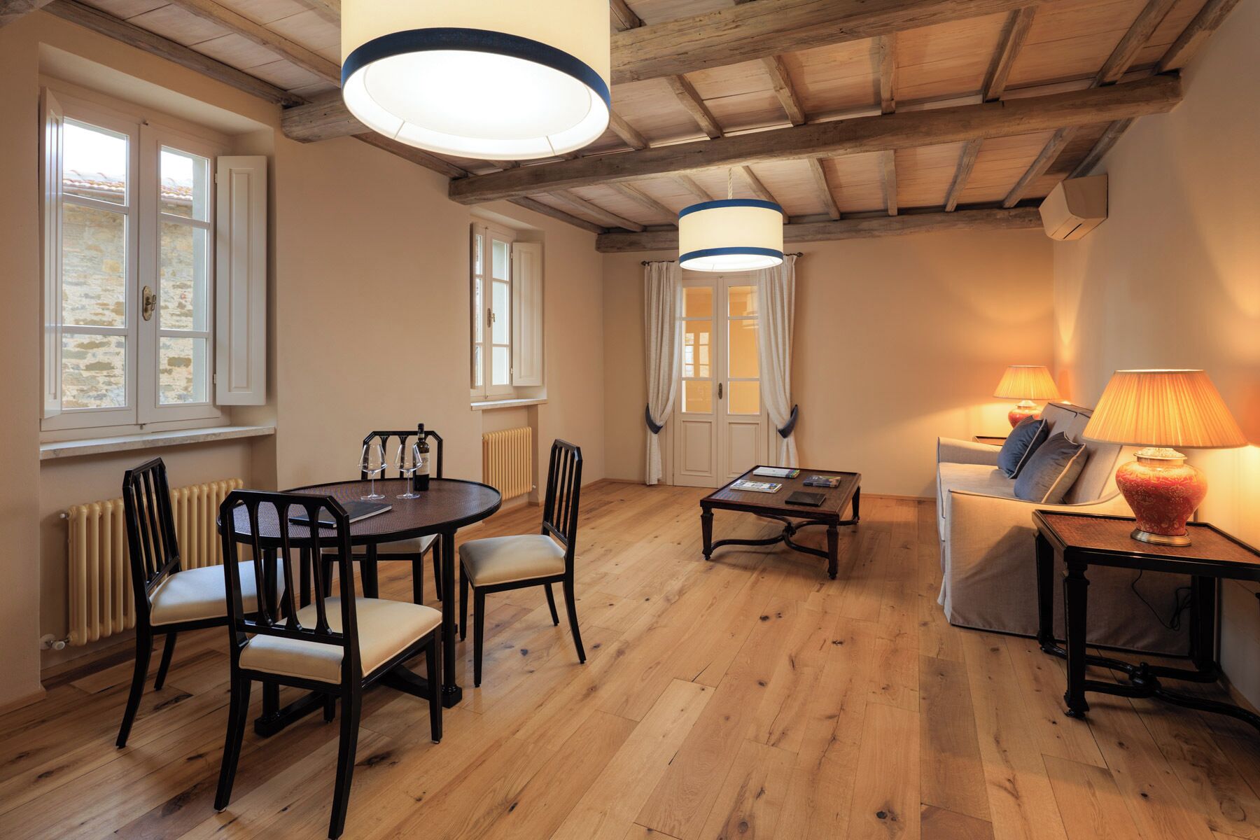 A room with a wooden floor, a dining table with chairs, a sofa, a lamp, and a radiator.