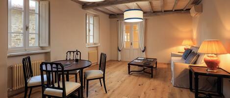 Una habitación con suelo de madera, una mesa de comedor con sillas, un sofá, una lámpara y un radiador.