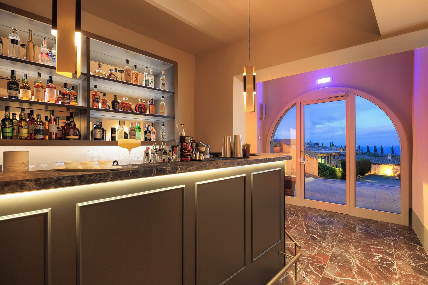 Zona de bar con estantes de botellas de licor, barra y vista a través de un ventanal.