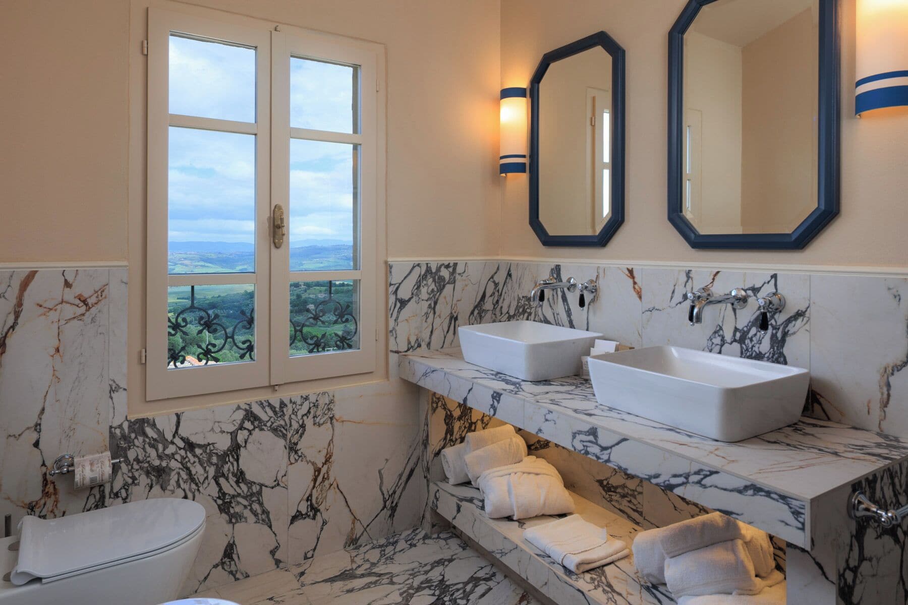 Ein Badezimmer mit zwei Waschbecken, einer Toilette, einem Fenster mit Blick und Marmorwänden.