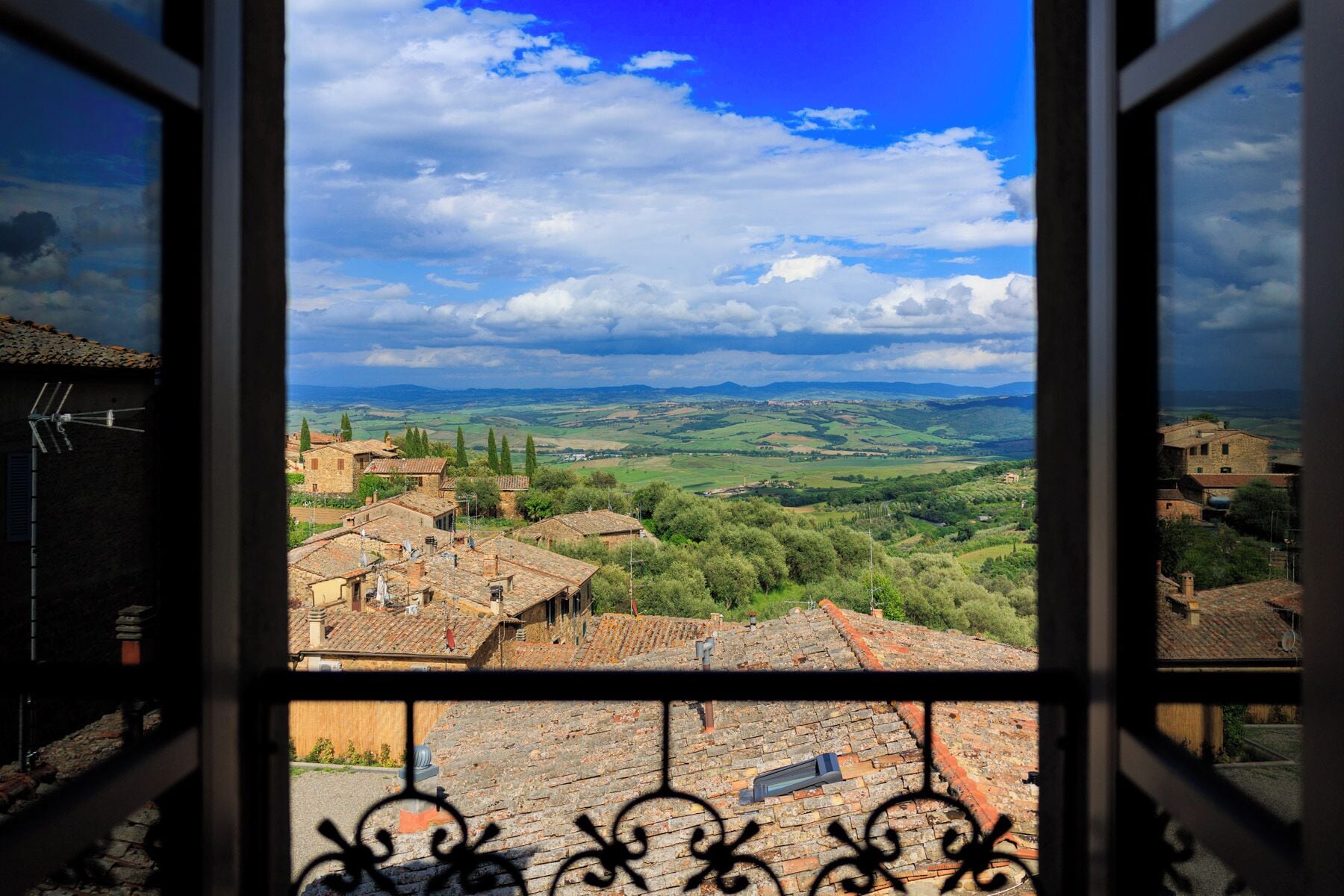 A view through a window of a town with traditional architecture, cobblestone streets, and a rural landscape.