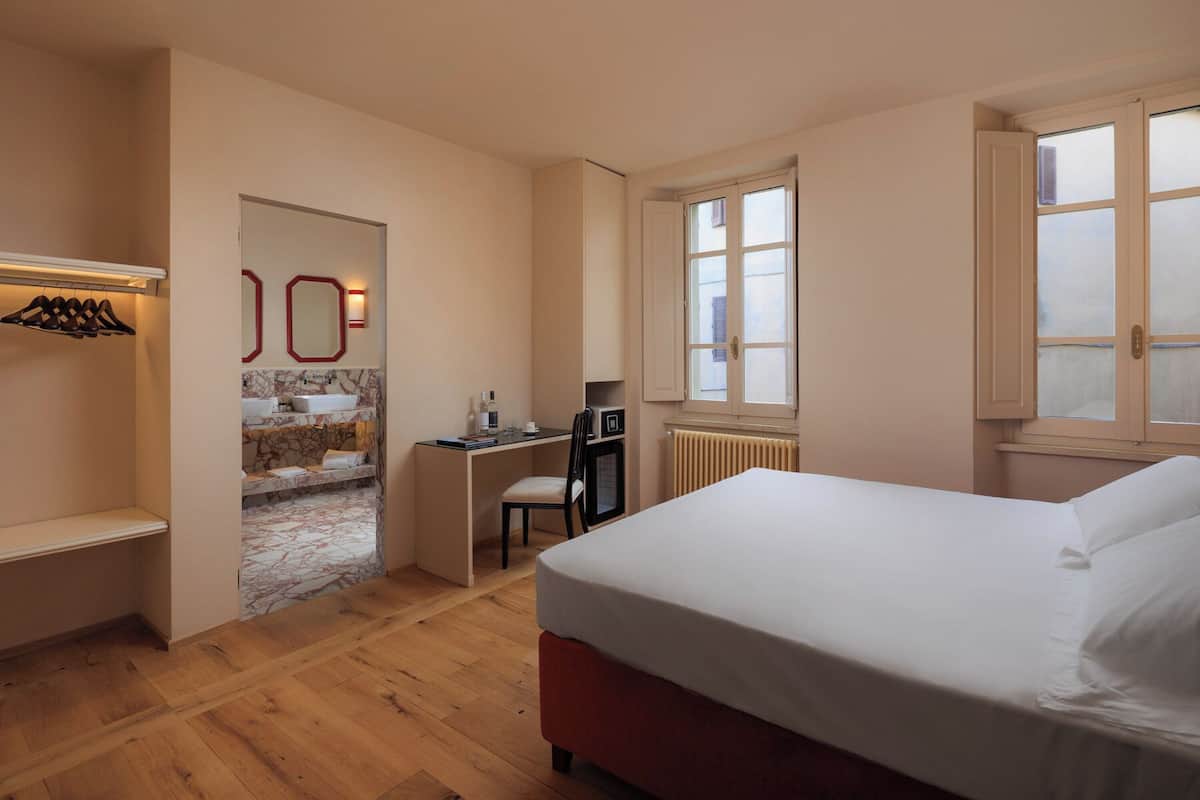 Ein Schlafzimmer mit Bett, Schreibtisch, Stuhl, Spiegel und einem Badezimmer inklusive Waschbecken und Handtuchhalter.