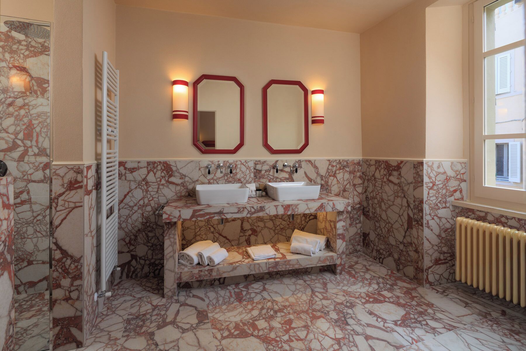 A bathroom with marble floors, two sinks, a towel rack, and a window.