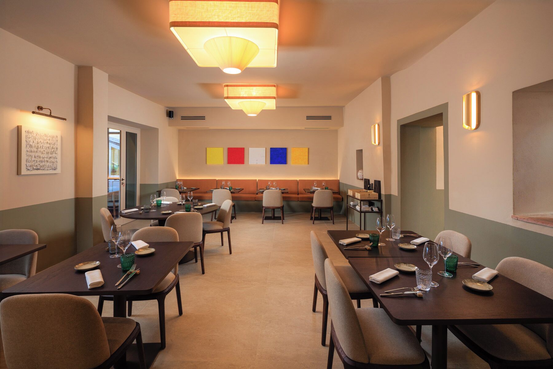 A dining area with tables set for meals, a seating area with a sofa, and a wall with colorful artwork.