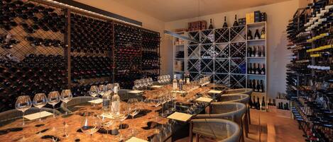 A wine cellar with a long table set for wine tasting, surrounded by wine racks and shelves.