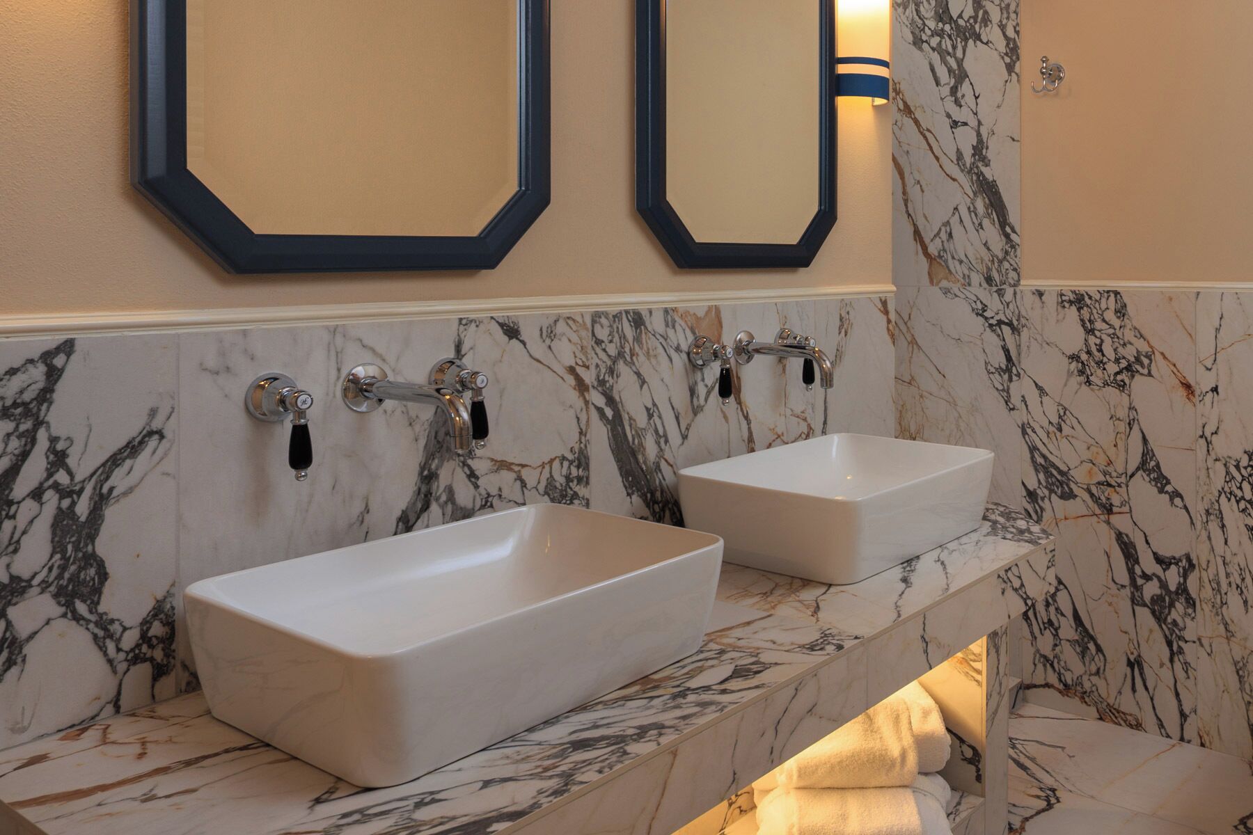 A bathroom with two white sinks, marble walls, and a towel rack.