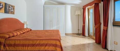 A hotel room with a large bed, a wardrobe, a door, a lamp, and a window with curtains.