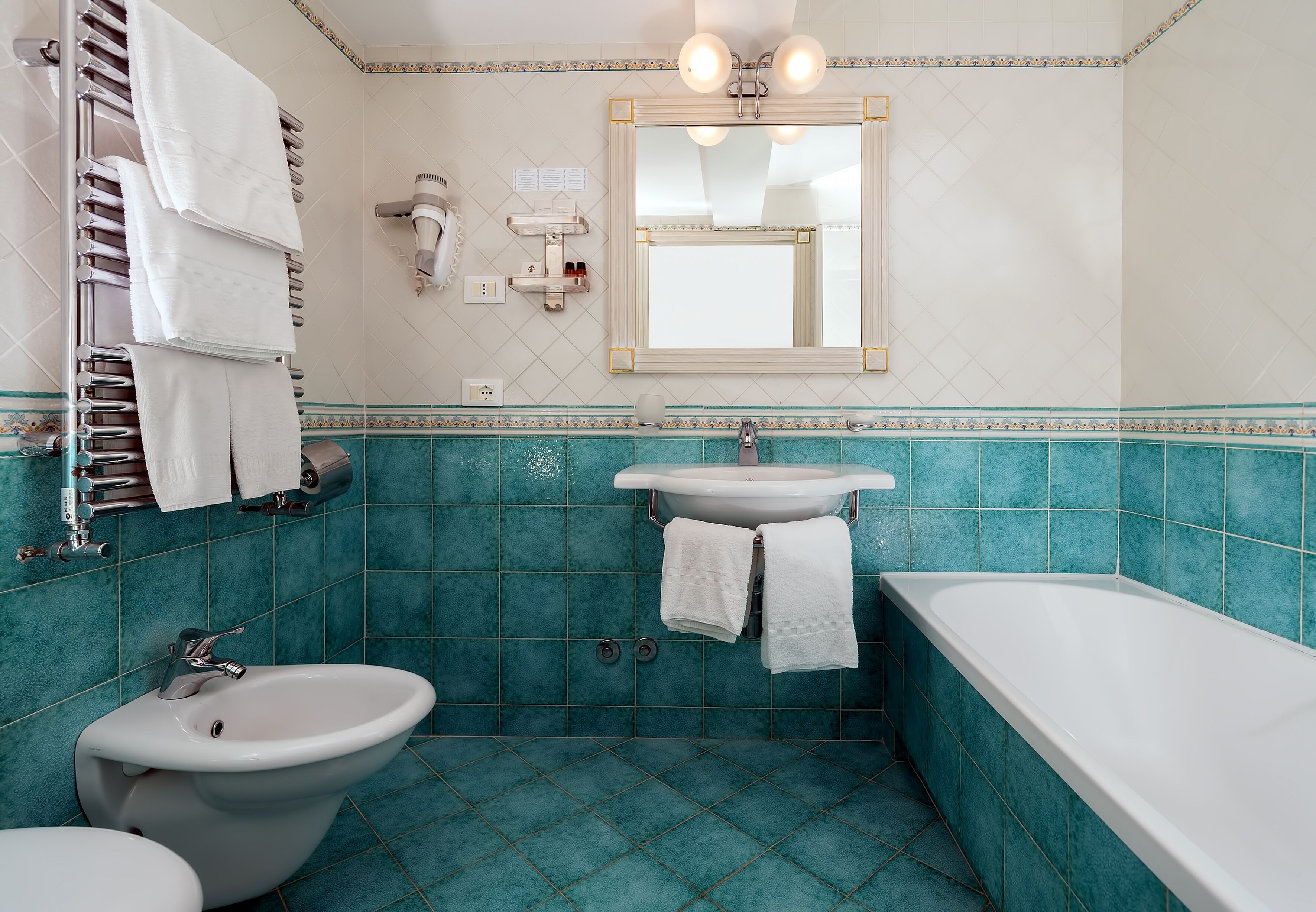 Et badeværelse med vask, bidet og badekar. Der er håndklæder på en håndklæderække, og et spejl over vasken.