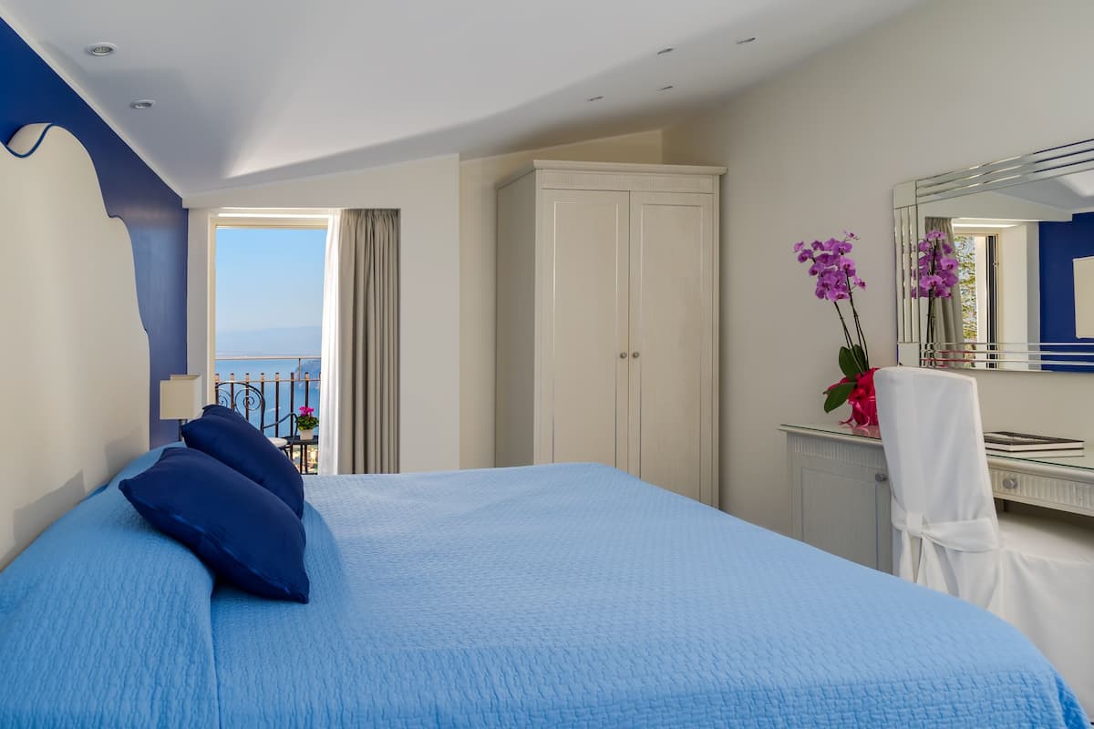 Quarto com cama grande, guarda-roupa, escrivaninha com espelho e vista para o mar.