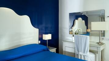 Camera d'albergo con un letto grande, una cassettiera, uno specchio e un comodino con una lampada.