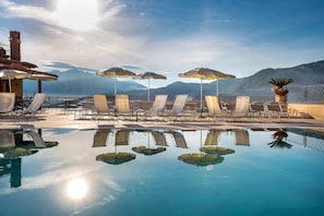 Ein Poolbereich mit Liegestühlen und Sonnenschirmen, umgeben von Bergen.