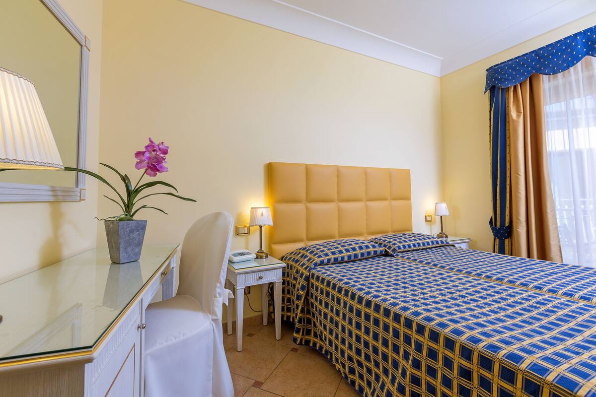 Quarto de hotel com cama, mesas de cabeceira, uma cadeira, abajur e planta em vaso.