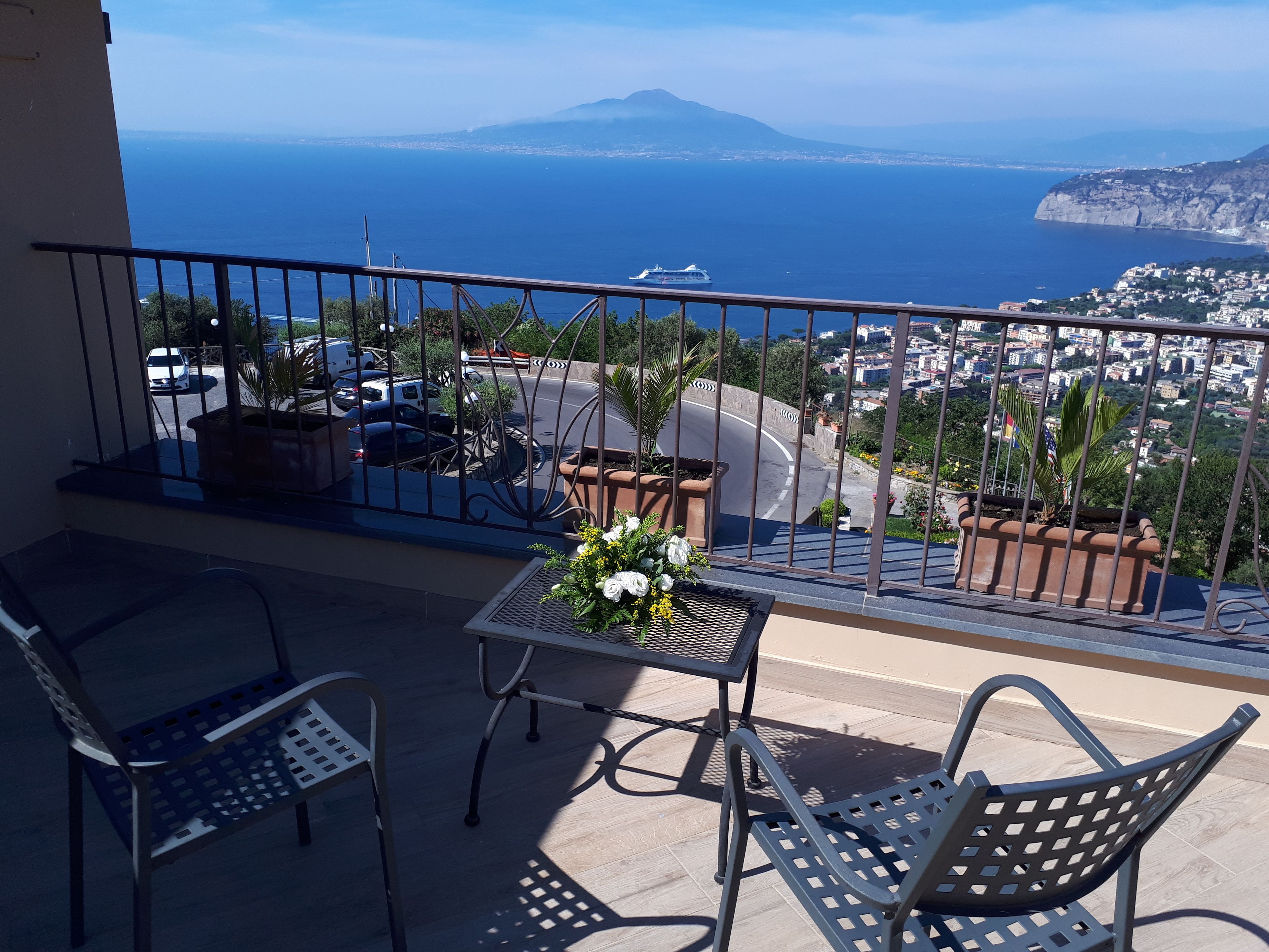 A balcony with a table and chairs, overlooking a coastal cityscape with a mountain in the distance.
