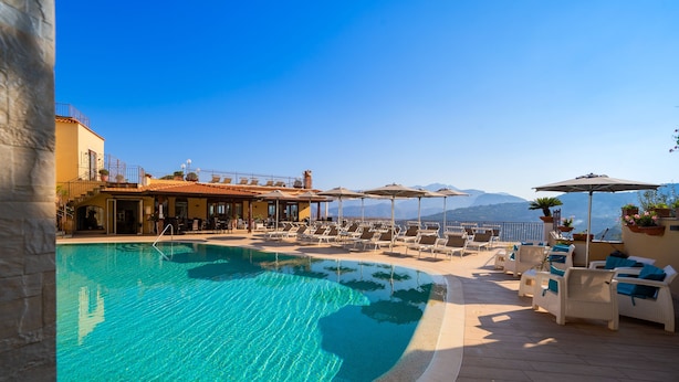 A poolside area with lounge chairs, umbrellas, and a view of mountains. - La Vue D'Or (Sorrento)