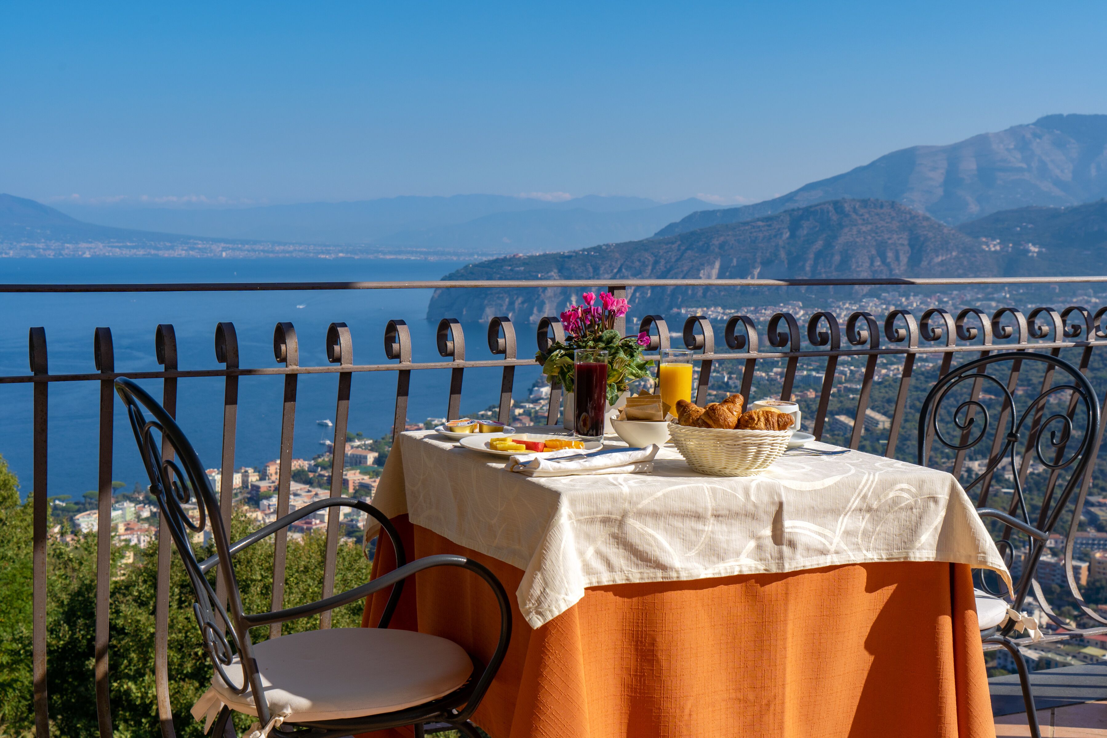 A table set with breakfast on a balcony overlooking a scenic coastal view.