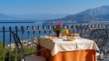 A table set with breakfast on a balcony overlooking a scenic coastal view.