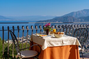 A table set with breakfast on a balcony overlooking a scenic coastal view.