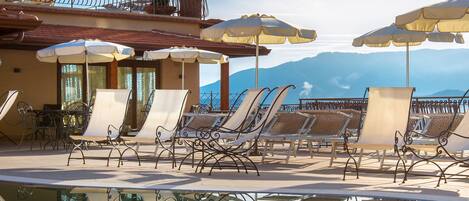 A poolside area with lounge chairs and umbrellas, a clear sky, and a mountain view.