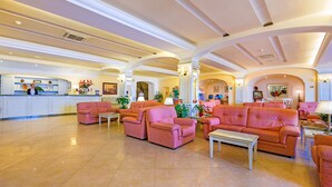 A spacious lobby with pink sofas and armchairs, a reception desk, and a kitchen area in the background. - La Vue D'Or (Sorrento)