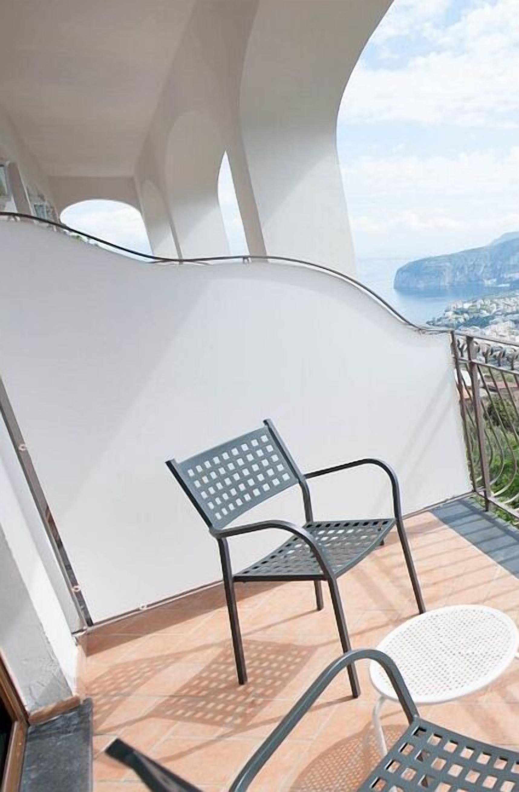 Ein Balkon mit Blick auf eine Küstenlandschaft, mit einem Metallstuhl und einem kleinen runden Tisch.