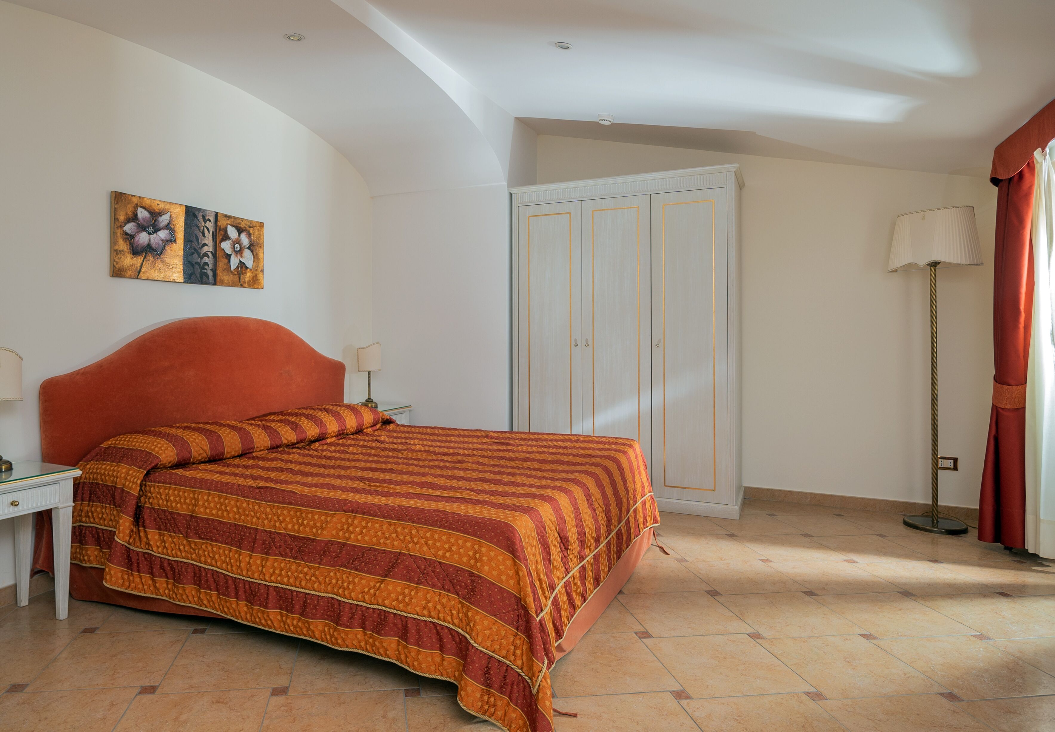 Une chambre à coucher avec un lit, une table de chevet, une lampe, une armoire et un tableau accroché au mur.