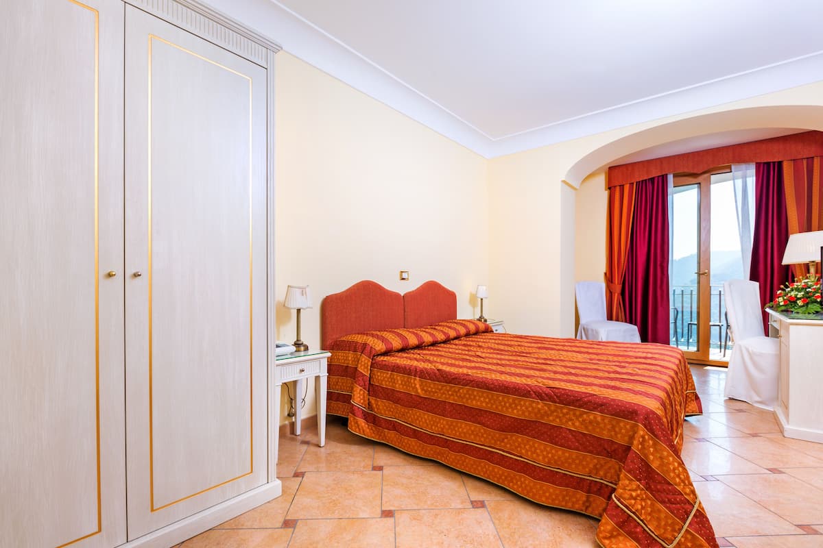 Quarto de hotel com uma cama grande, uma escrivaninha com luminária, uma cadeira e vista para o exterior.