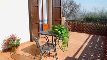 Un patio con tavolo e sedie, una pianta in vaso e vista su alberi e una recinzione.