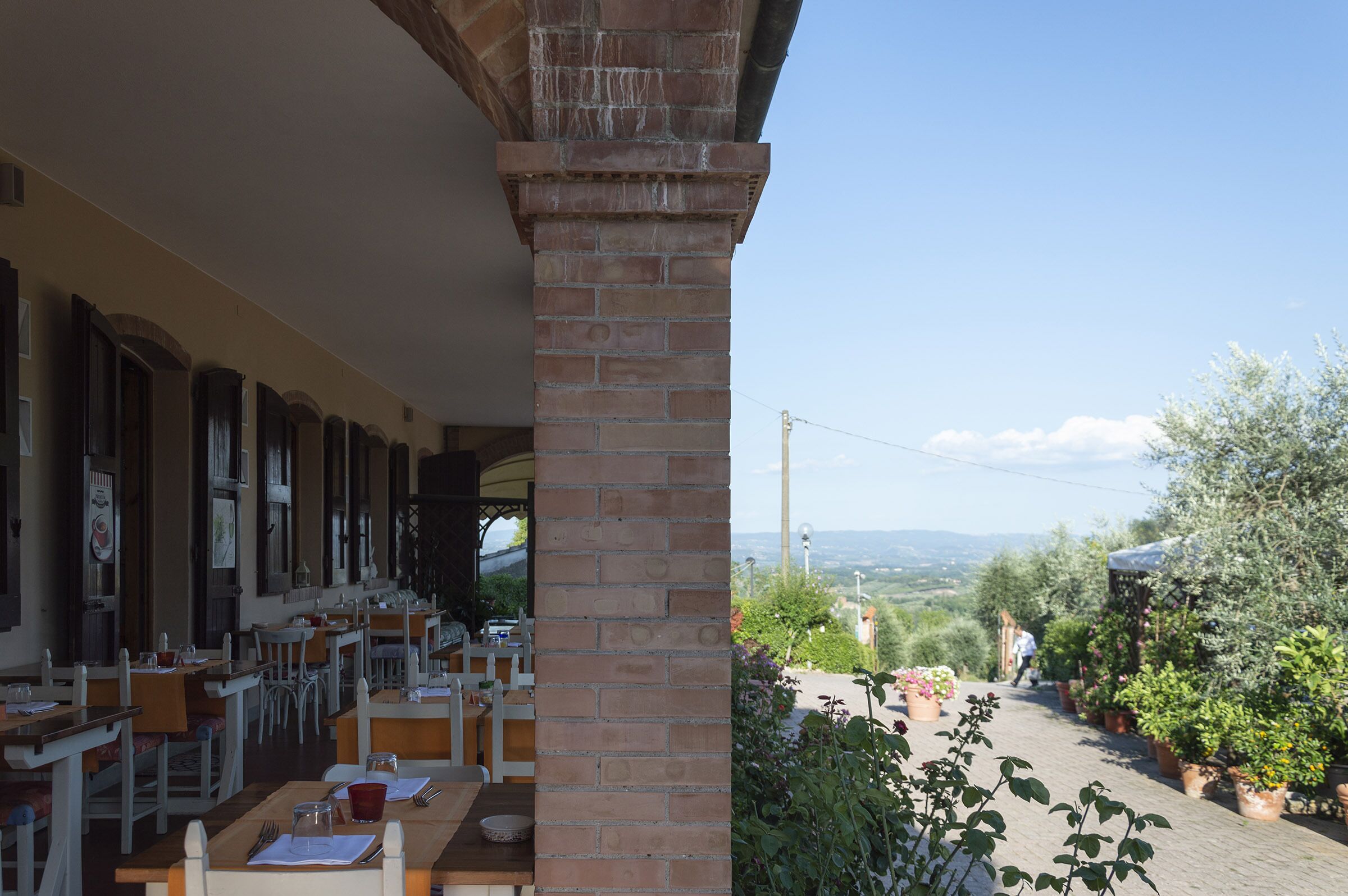 A restaurant with outdoor seating, brick columns, and a view of the countryside.