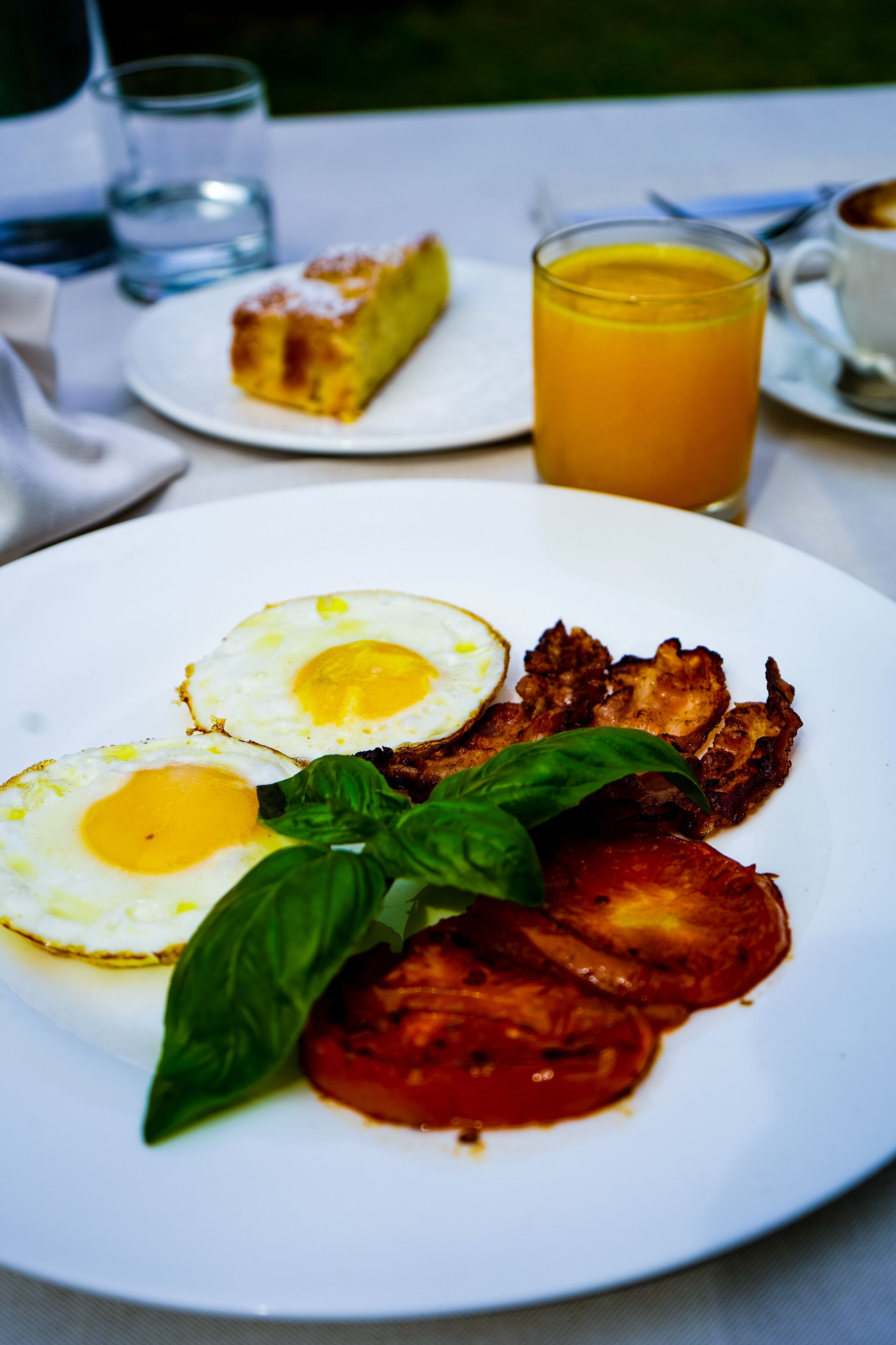 A breakfast plate with eggs, bacon, tomato, and basil.